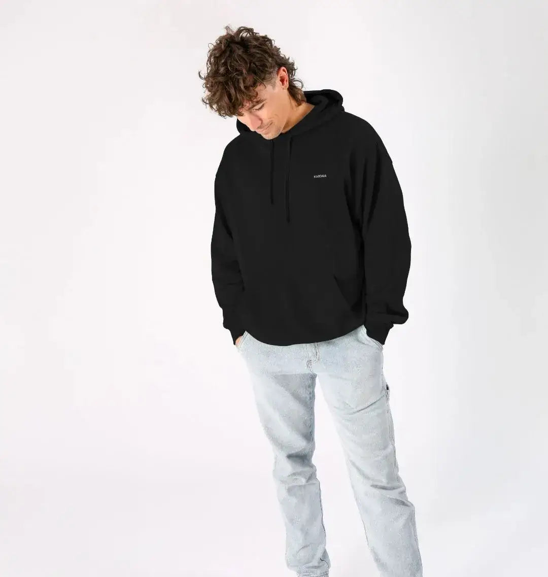 Homme portant un hoodie noir KARDAIA avec un jean clair, vu de face, regard vers le bas