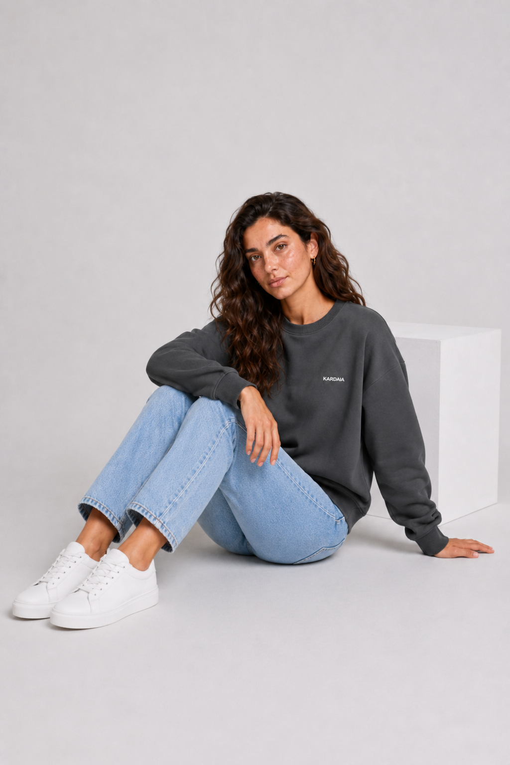Femme assise portant un pull oversize gris charbon en coton biologique avec un jean clair