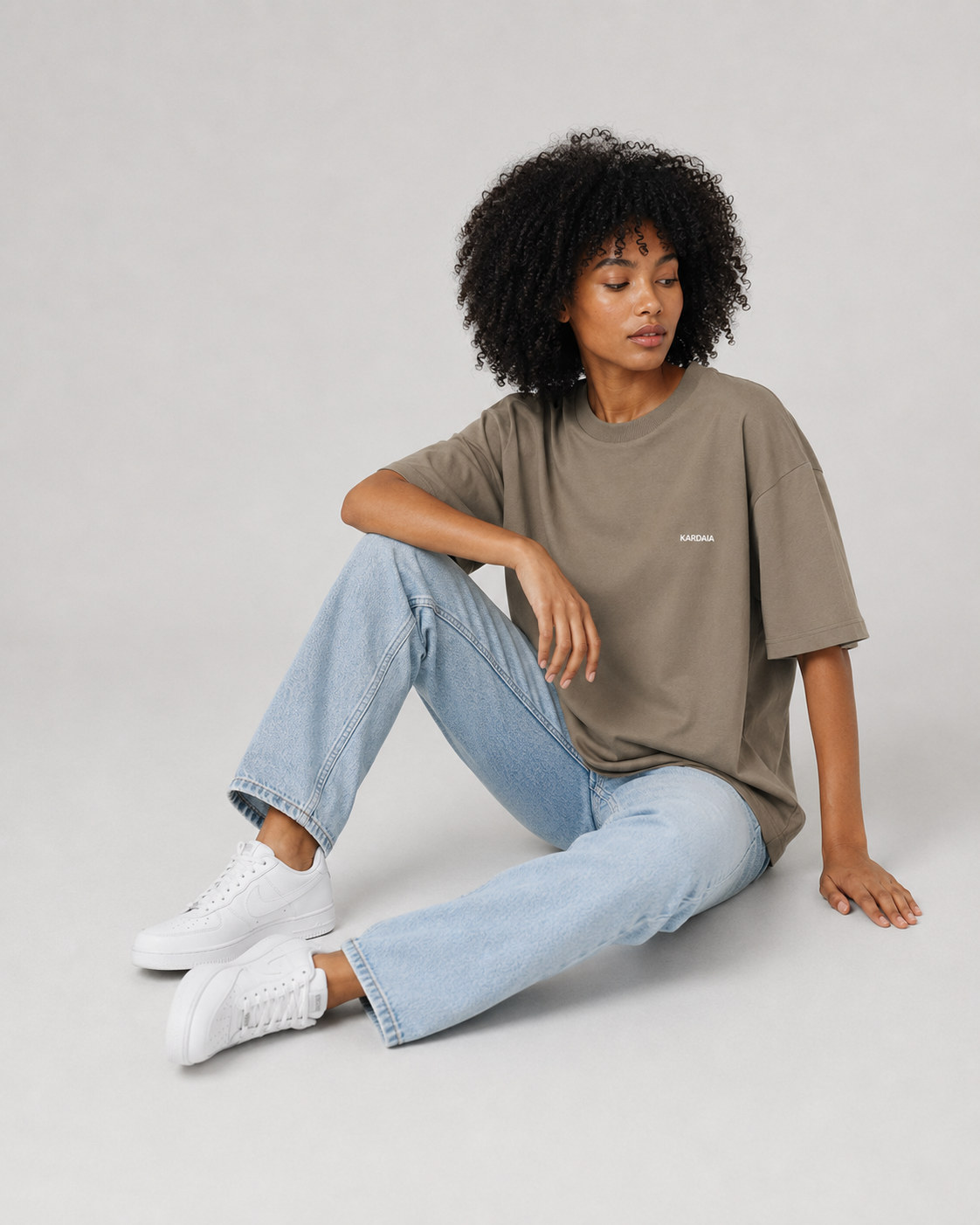 Femme assise portant un t-shirt oversize taupe en coton biologique avec un jean clair