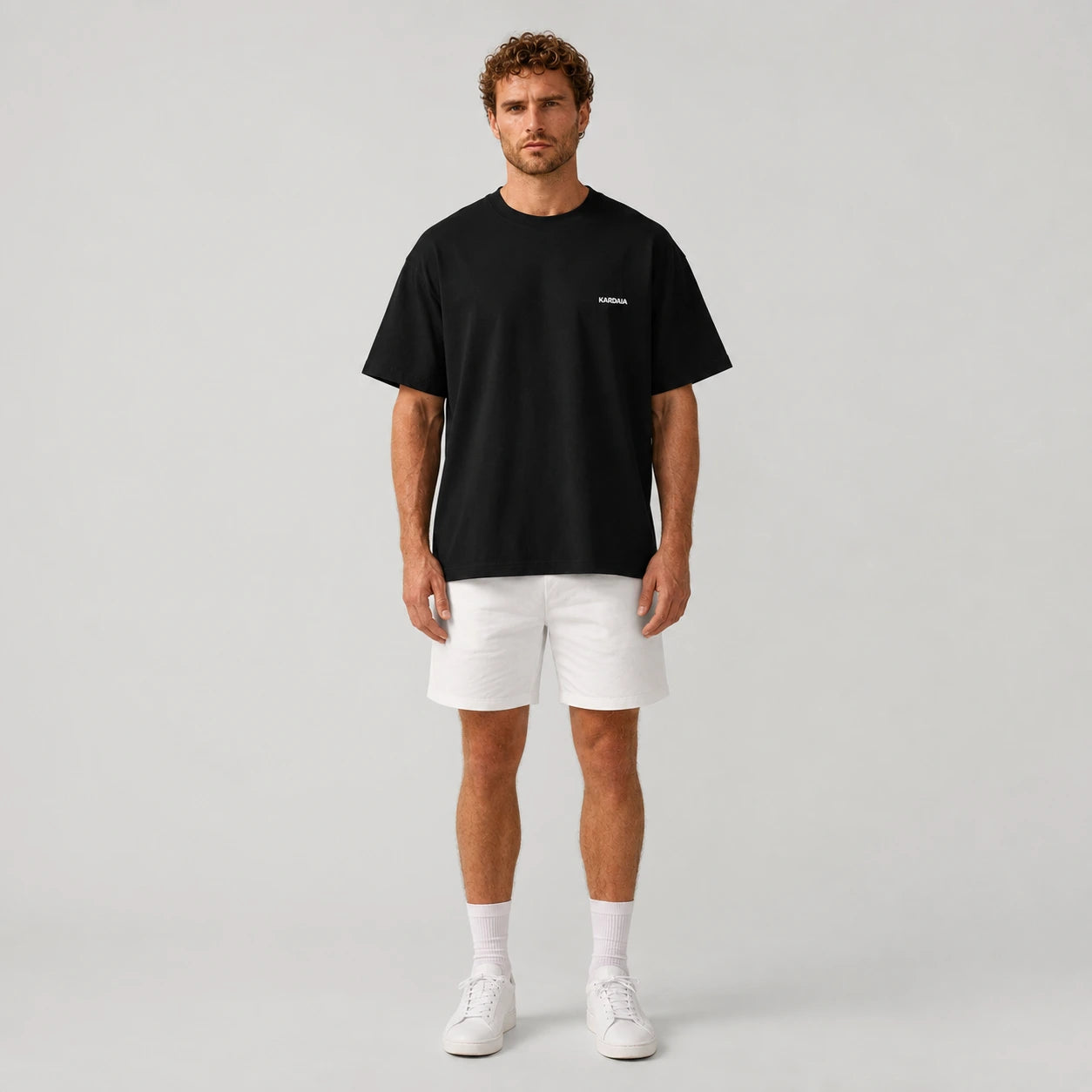 T-shirt oversize homme Kardaia noir en coton biologique, associé à un short blanc pour une silhouette contrastée. La vue de face met en évidence sa coupe large, son col rond et sa longueur confortable.