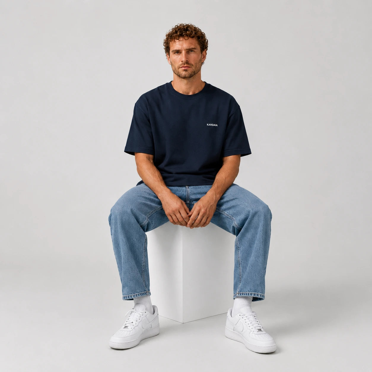 T-shirt oversize homme Kardaia bleu marine en coton biologique, photographié en position assise. La posture permet d’observer le volume de la coupe, la longueur des manches et le tombé naturel du tissu.