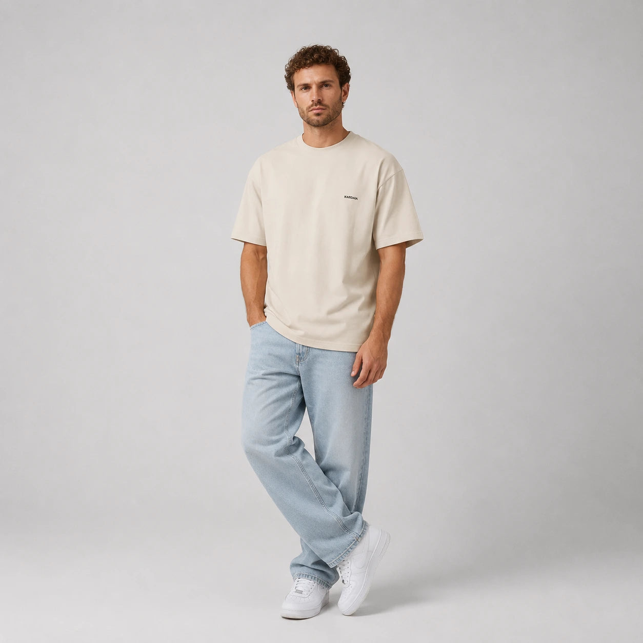 T-shirt oversize homme Kardaia écru en coton biologique, présenté avec un jean bleu clair et des baskets blanches. La vue en pied met en valeur sa coupe ample, ses manches larges et ses épaules légèrement tombantes.