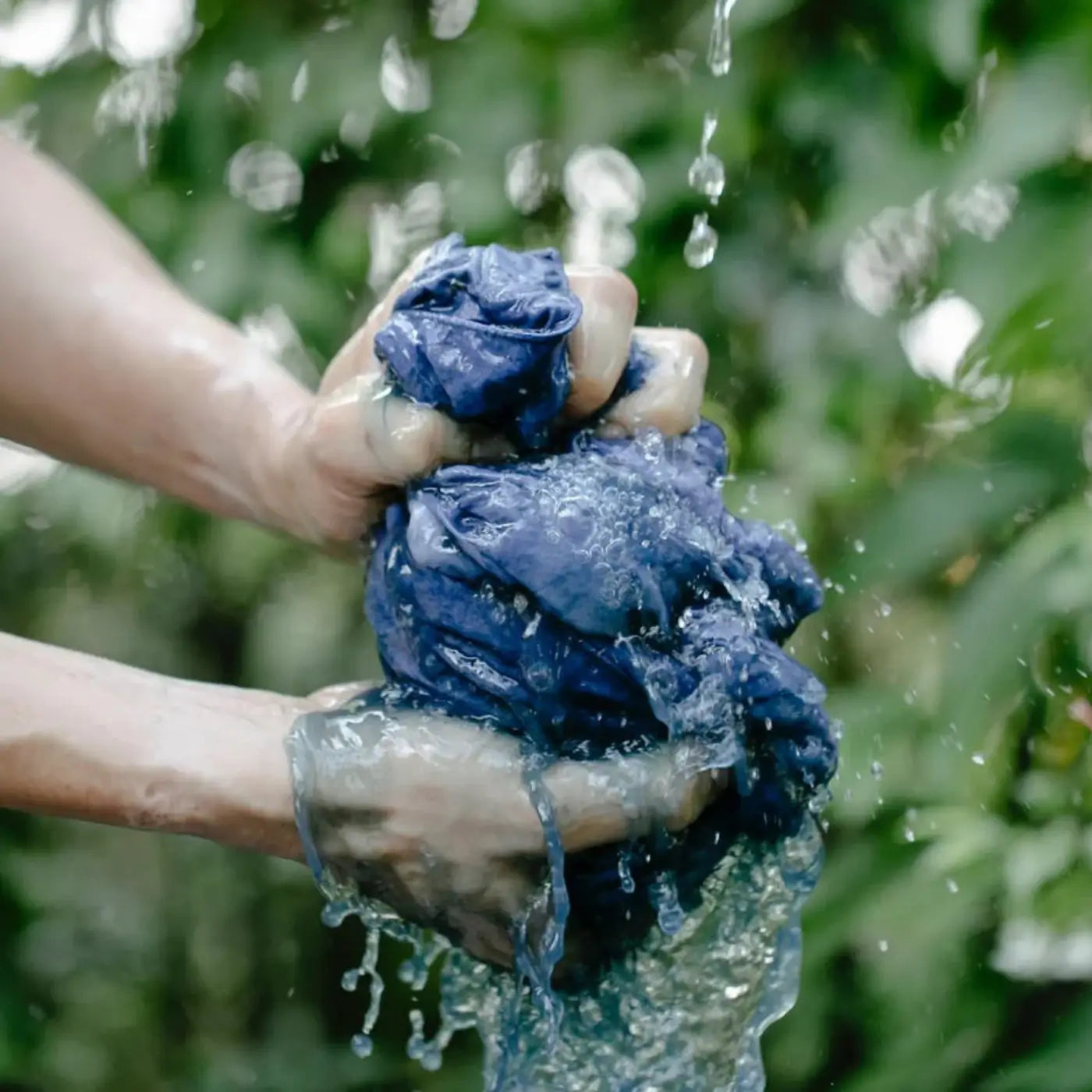 Lavage à la main d’un vêtement en coton bleu, avec de l’eau ruisselant entre les doigts