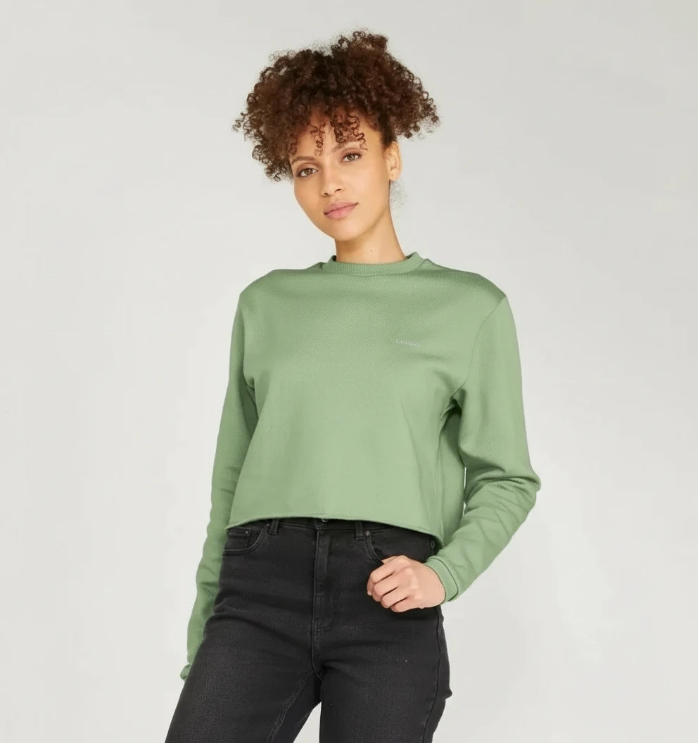 Femme portant un pull boxy vert argile en coton bio, coupe ample, associé à un jean noir.