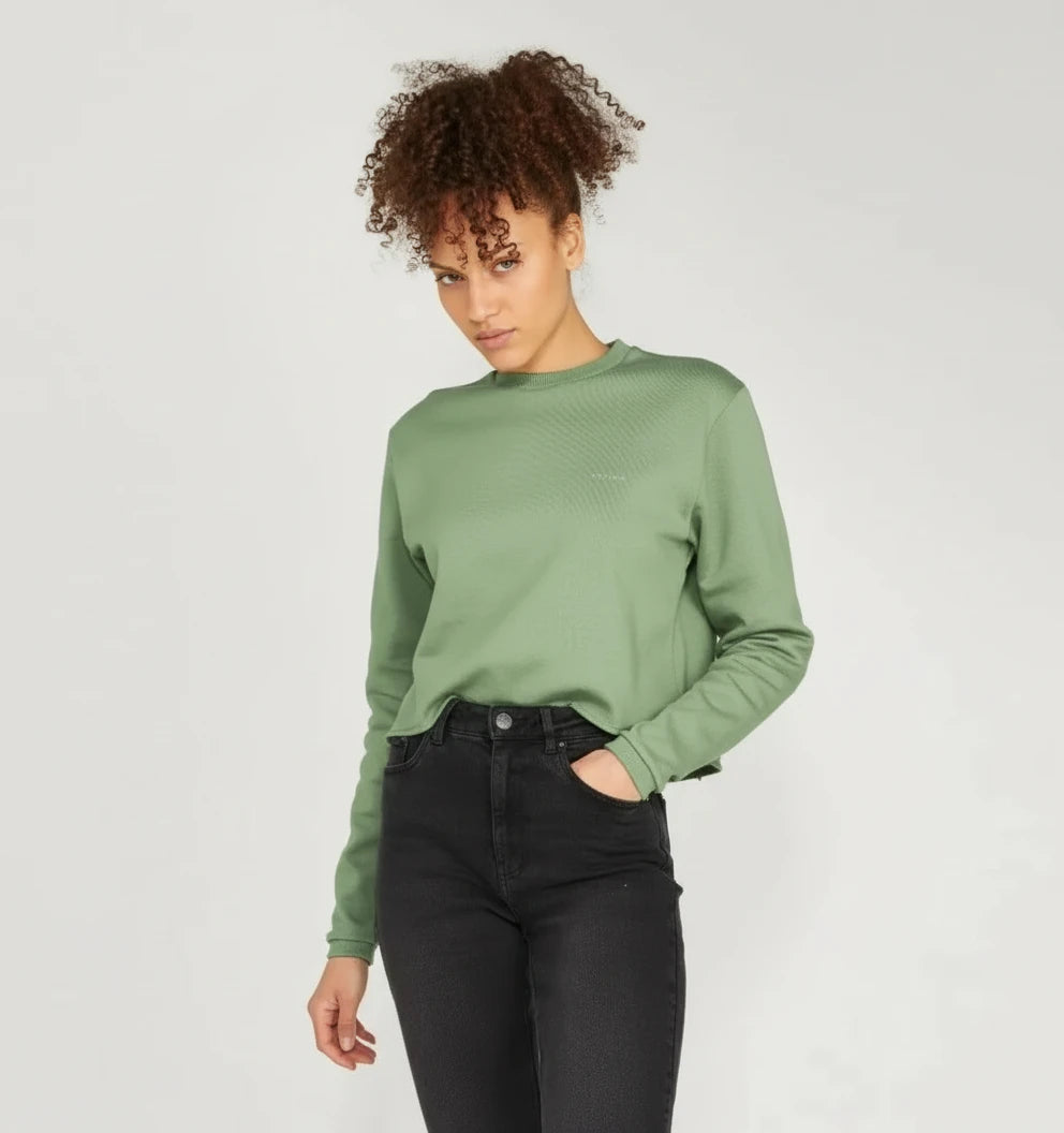Pull boxy femme vert argile vu de profil, coupe courte et ample, mannequin souriant en jean noir.