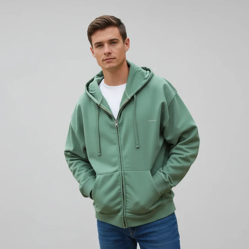 homme portant un sweat zippé vert argile KARDAIA sur la plage, posture décontractée et naturel