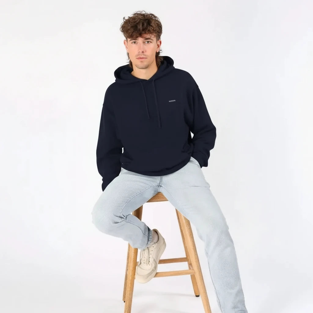 Homme assis sur un tabouret, portant un hoodie bleu marine KARDAIA avec jean clair et baskets