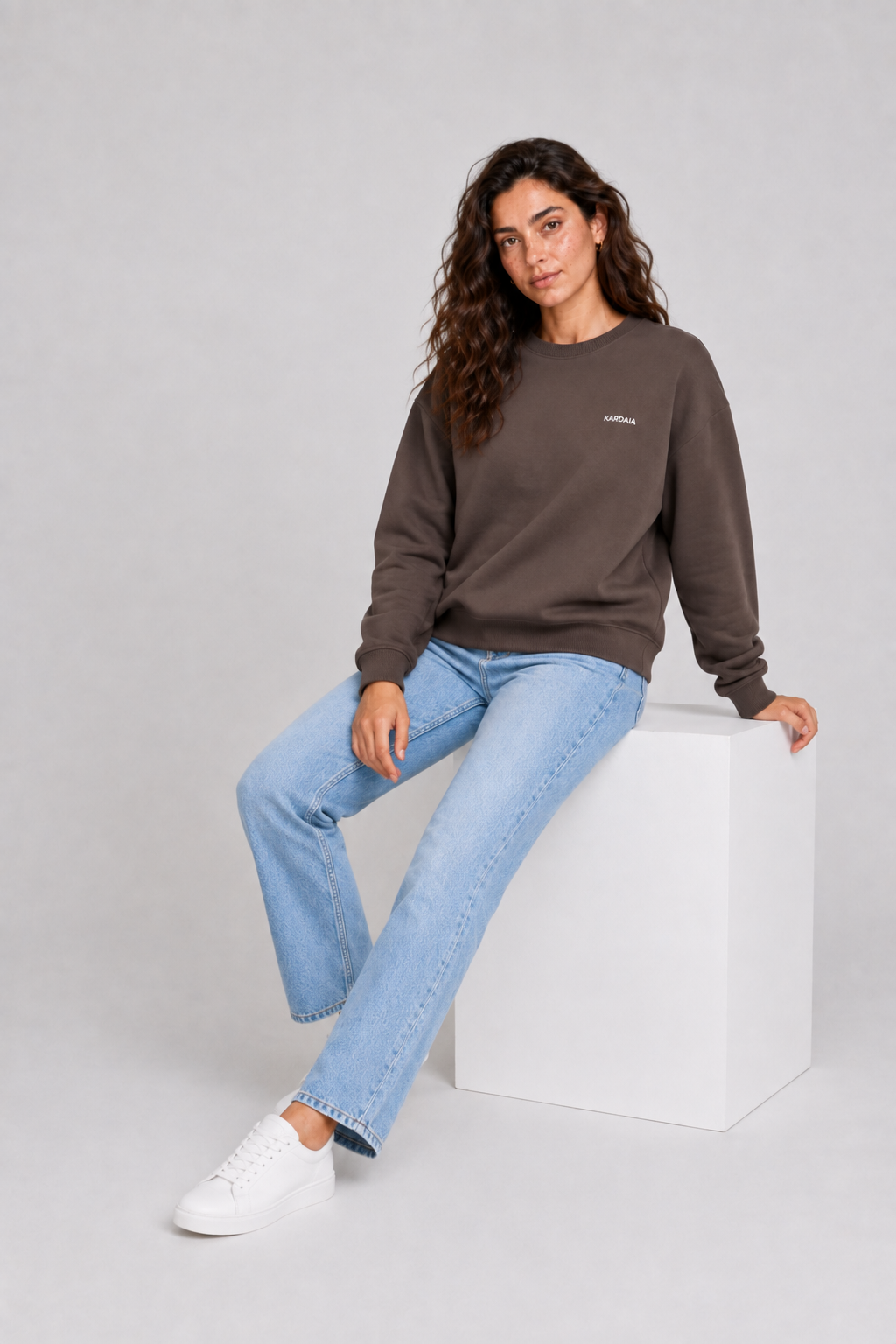 Pull oversize brun pour femme en coton biologique présenté assise avec un jean clair