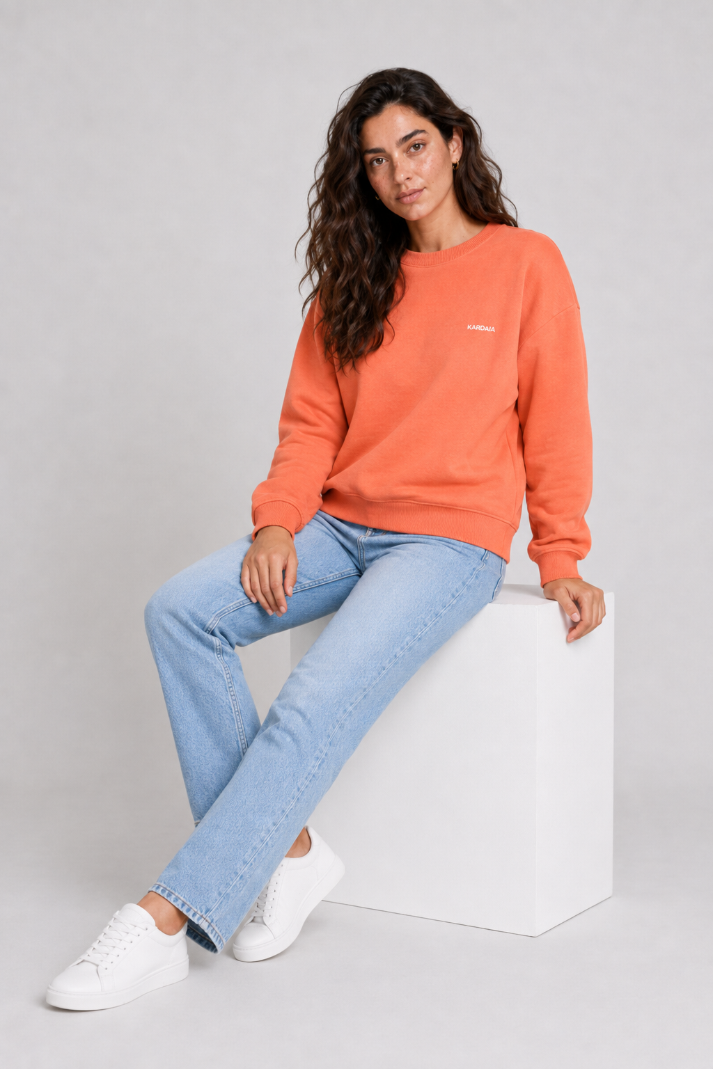 Femme assise portant un pull oversize orange en coton biologique avec un jean bleu