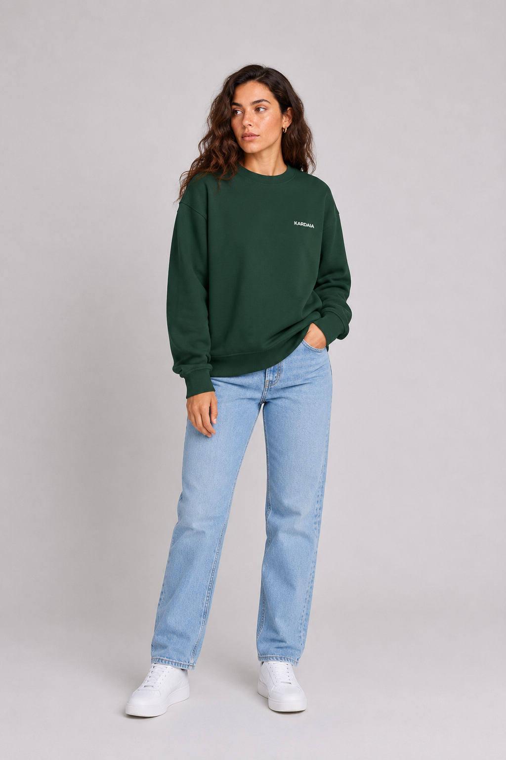 Femme portant un pull oversize vert foncé en coton biologique avec un jean bleu clair