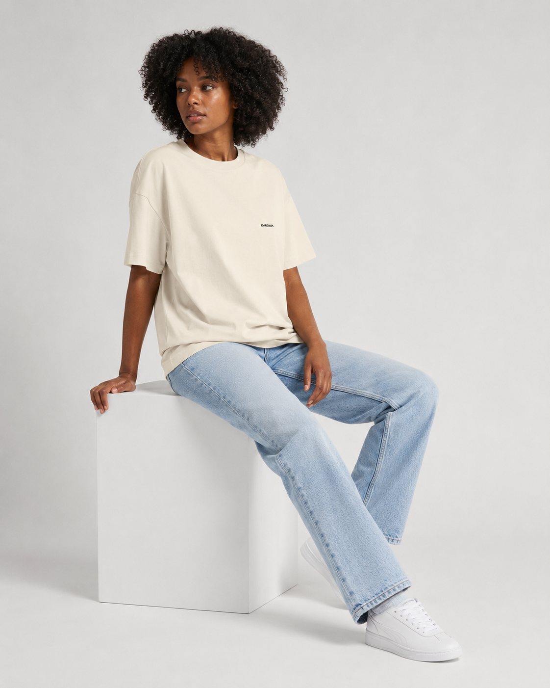 Femme assise portant un t-shirt oversize écru en coton biologique avec un jean bleu clair