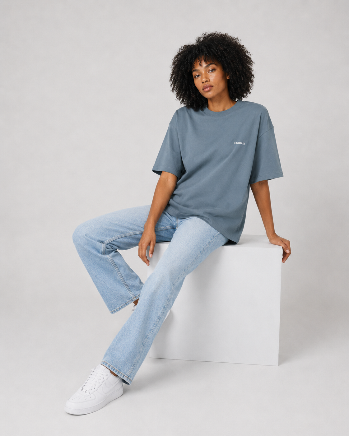 Femme assise portant un t-shirt oversize bleu ardoise en coton biologique avec un jean bleu clair