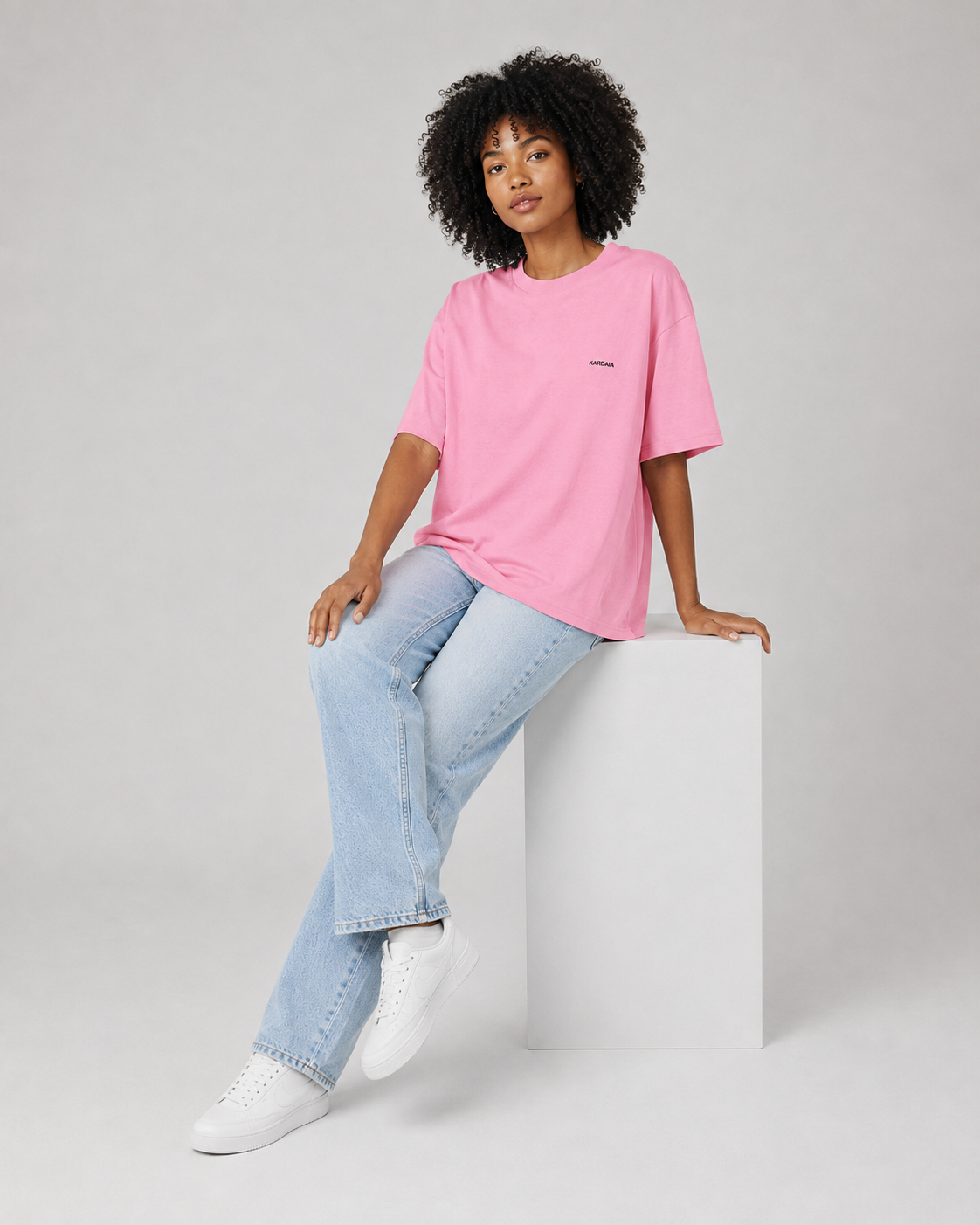 Femme assise portant un t-shirt oversize rose en coton biologique avec un jean bleu clair