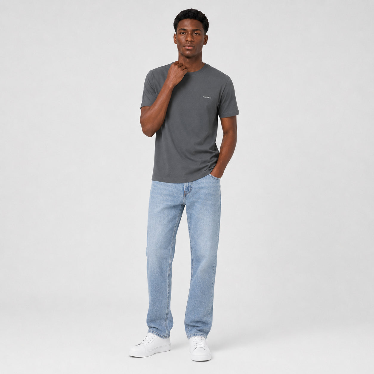 T-shirt homme Kardaia gris anthracite en coton biologique, présenté avec un jean bleu clair et des baskets blanches. Sa coupe droite, son col rond et sa couleur neutre en font une pièce facile à associer au quotidien.