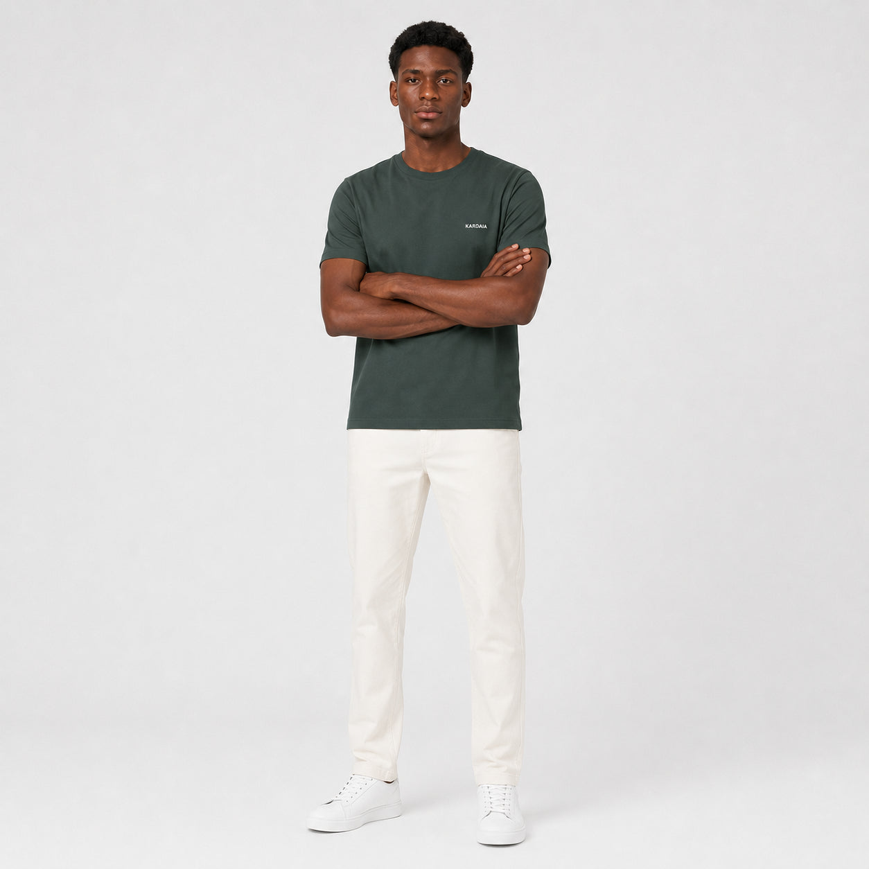 T-shirt homme Kardaia gris foncé en coton biologique, photographié de face avec les bras croisés. Sa coupe classique et sa teinte profonde sont associées à un pantalon écru pour une silhouette sobre et naturelle.