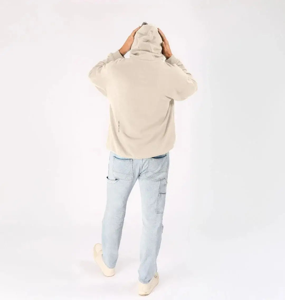 Homme vu de dos portant un sweat KARDAIA avoine avec un jean clair et capuche relevée
