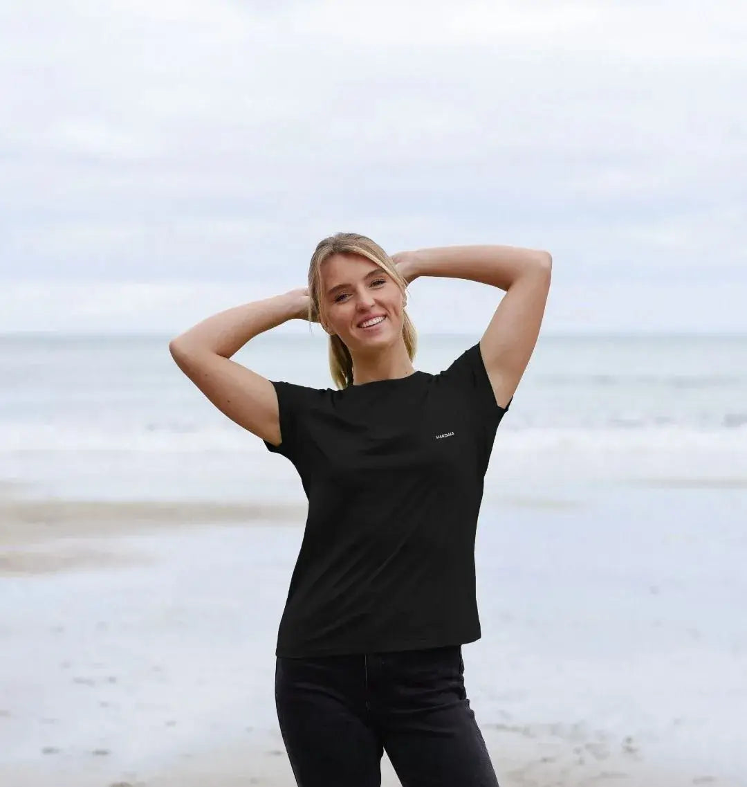 femme portant un t-shirt noir basalte KARDAIA sur la plage, look naturel et épuré